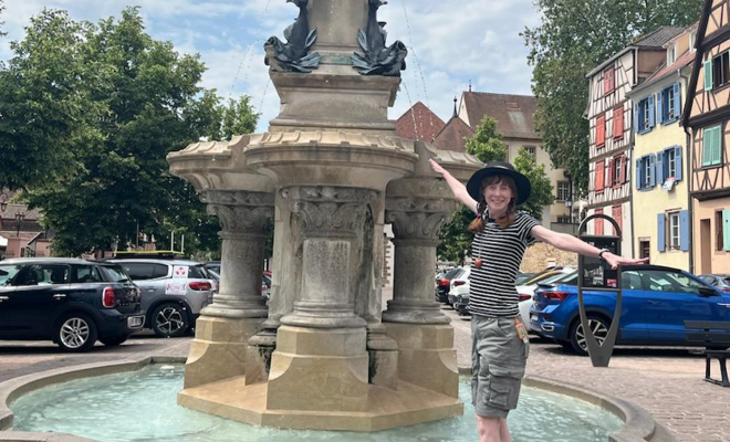 Rebecca standing in a decorative fountain while traveling abroad, holding her arms out and smiling