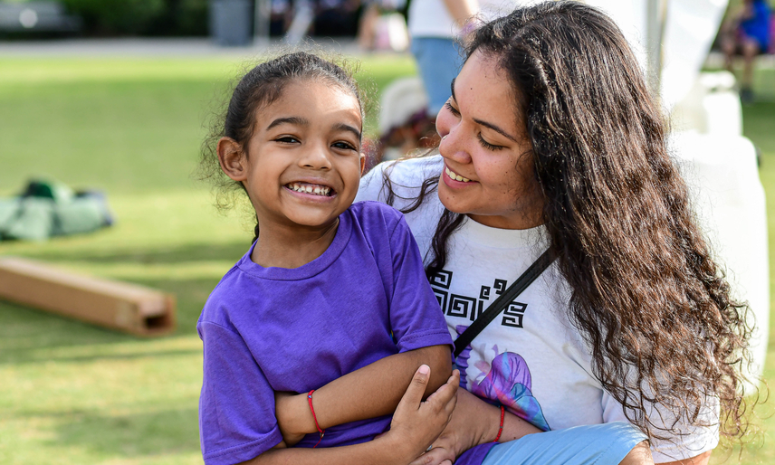 young child in purple shirt smiling next to mother looking down and smiling at her