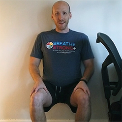 A BreatheStrong+ participant doing a wall sit while wearing a BreatheStrong+ t-shirt