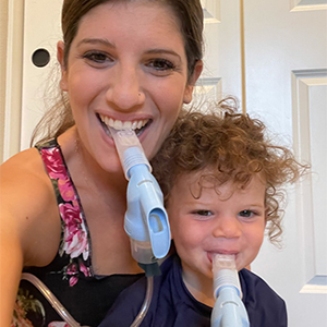 A photovoice study participant using her nebulizer while her toddler sits in her lap holding a nebulizer