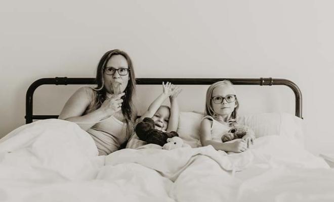 Jessica doing her breathing treatments in her bed with her two young daughters next to her.