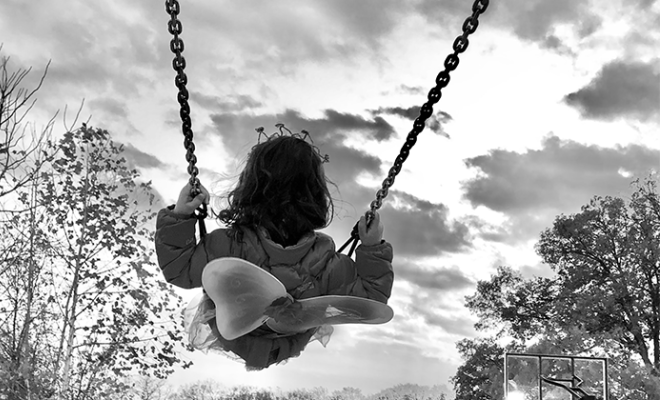Black and white photo of a girl on a swing set in a butterfly costume.