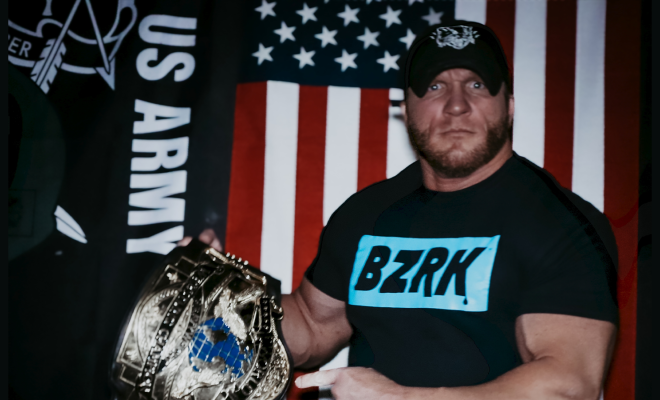 Dustin Raynor holding a wrestling belt and posing in front of an American flag