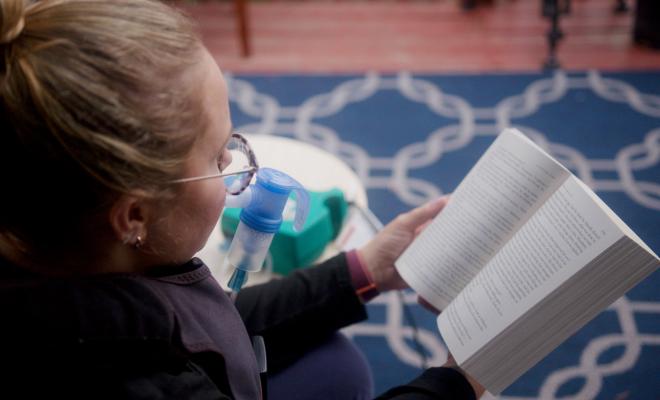 An adult with CF reading a book while using her vest and nebulizer