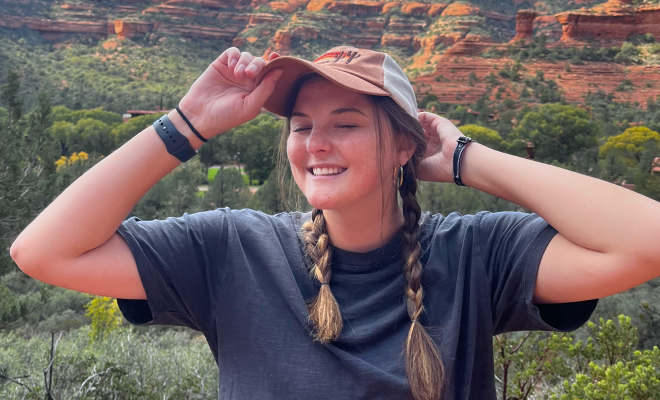 Christa Lux smiling and grabbing her hat in front of the Grand Canyon
