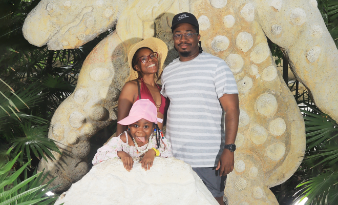 Annette smiling and posing with her husband and daughter in front of a statue.