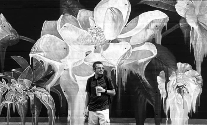 A black-and-white photo of Schyler standing in front of a mural of flowers